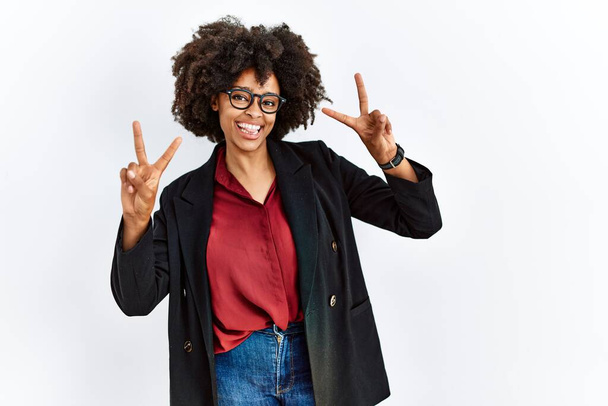 Африканская американка с афроволосами в деловой куртке и в очках, улыбающихся языком, показывает пальцы обеих рук, делающих знак победы. Номер два.  - Фото, изображение