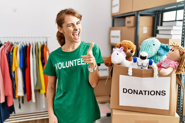 Beautiful caucasian woman wearing volunteer t shirt at donations stand pointing fingers to camera with happy and funny face. good energy and vibes.  - Photo, Image