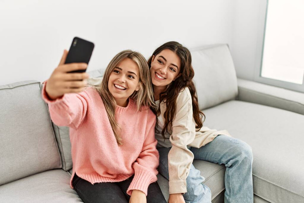 Młoda para uśmiecha się szczęśliwy robiąc selfie przez smartfona w domu. - Zdjęcie, obraz