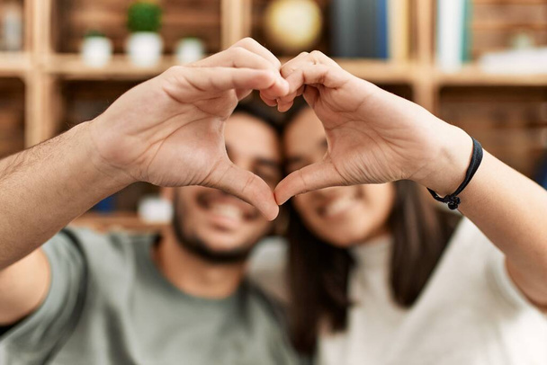 Молодая латинская пара улыбается счастливой делая символ сердца с руками дома. - Фото, изображение