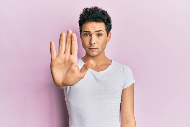 Young handsome man wearing casual white t shirt doing stop sing with palm of the hand. warning expression with negative and serious gesture on the face.  - Photo, image