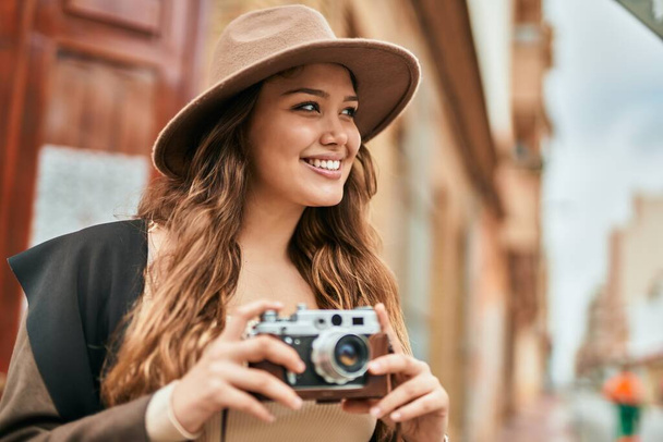 Mladá hispánská turistka se šťastně usmívá pomocí vintage kamery ve městě. - Fotografie, Obrázek