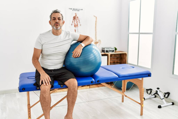 Middle age hispanic man at pain recovery clinic holding pilates ball looking at the camera blowing a kiss on air being lovely and sexy. love expression.  - Valokuva, kuva