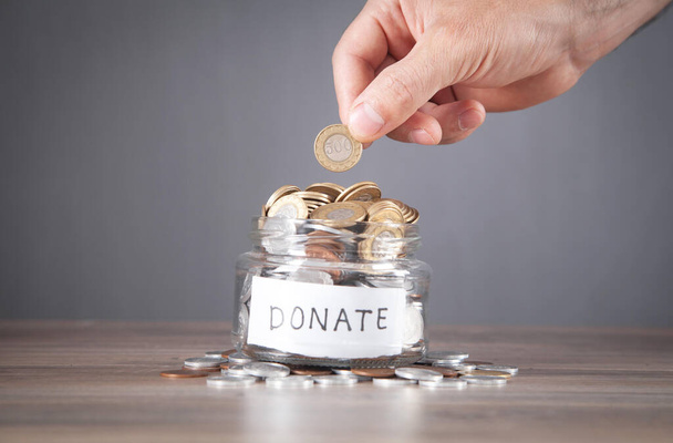 Male hand putting coin into Donation jar. - Foto, afbeelding