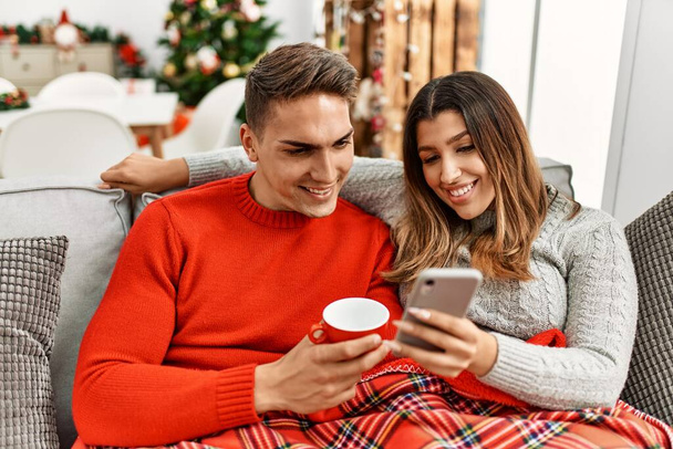 Mladý pár používá smartphone a pije kávu. Sedět doma na gauči. - Fotografie, Obrázek