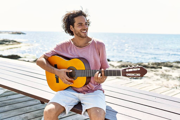 Genç İspanyol adam klasik gitar çalıyor sahilde bankta oturuyor.. - Fotoğraf, Görsel