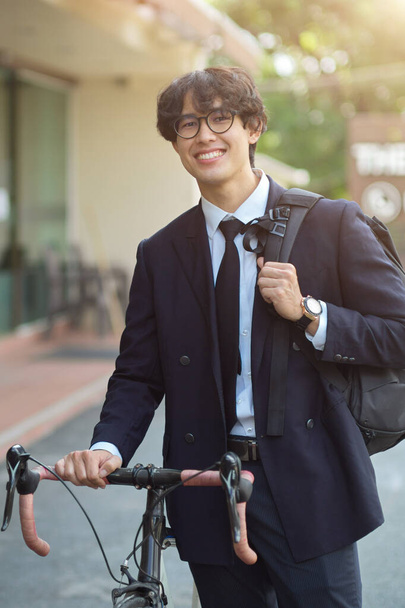 Ritratto di allegro uomo d'affari millenario in giacca e cravatta che cammina con la bicicletta per strada. - Foto, immagini