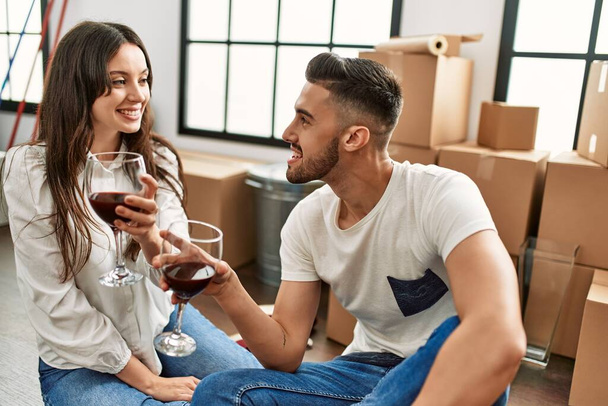 Joven pareja hispana sonriendo feliz brindis con vino tinto en nuevo hogar. - Foto, imagen