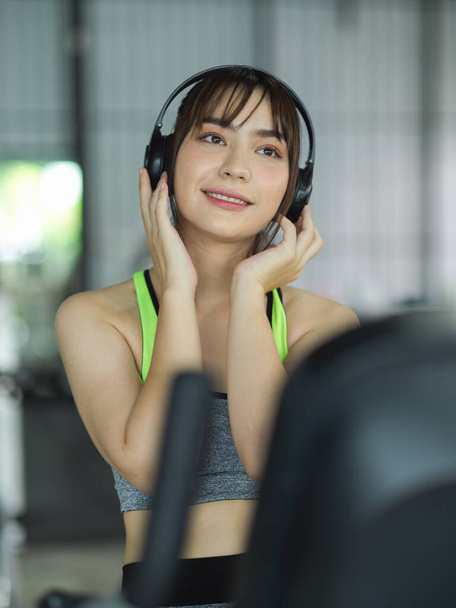 Charmante Fitness-Frau hört Musik über ihren drahtlosen Kopfhörer, während sie auf dem Laufband trainiert. - Foto, Bild