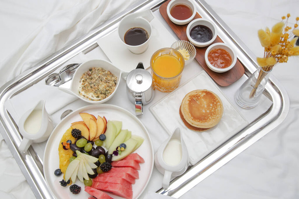 Frühstück Tablett im Bett in Luxus-Resort. Frühstück im Bett mit Obst, Pfannkuchen, Müsli, Kaffee und Saft auf einem Tablett. - Foto, Bild