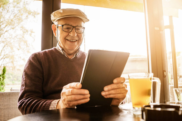 Uomo anziano è seduto in caffè e utilizzando tablet digitale. - Foto, immagini
