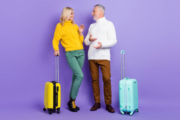 Photo of charming pretty senior husband wife dressed knitwear sweaters holding luggage communicating isolated violet color background - 写真・画像