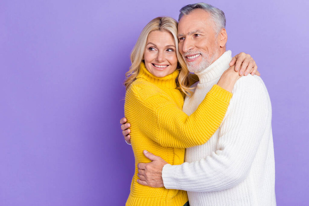 Photo of funny sweet senior husband wife dressed knitwear sweaters hugging looking empty space smiling isolated violet color background - Foto, Imagem