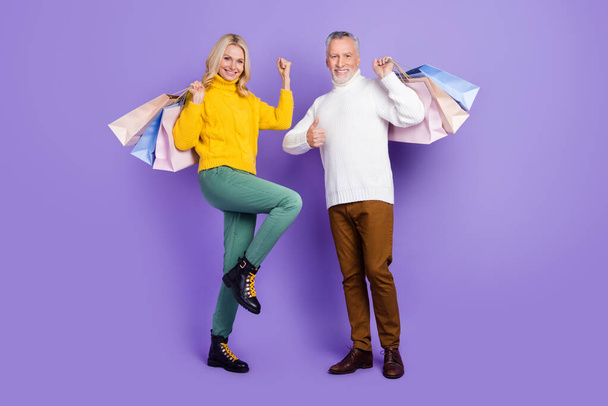 Photo of shiny lucky mature wife husband wear knitted pullovers smiling holding bargains rising fists isolated purple color background - Fotoğraf, Görsel