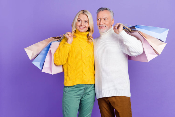 Photo of adorable dreamy senior husband wife dressed knitwear sweaters hugging holding bags empty space isolated violet color background - Fotoğraf, Görsel
