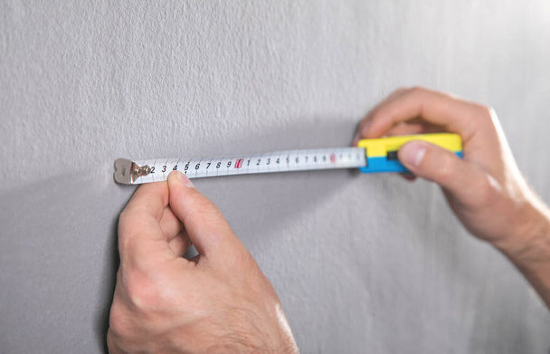 Человек измеряет серую стену измерительной лентой. - Фото, изображение