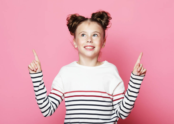 Funny little girl is surprised and shows her thumbs up, on a pink background - Photo, image