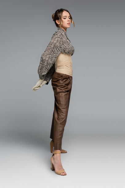 longitud completa de la mujer con estilo en blusa con estampado de cebra posando con las manos detrás de la espalda en gris - Foto, imagen