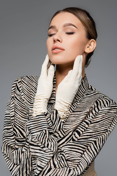 модная женщина в блузке с животным шрифтом и перчатками позирует изолированно на сером - Фото, изображение