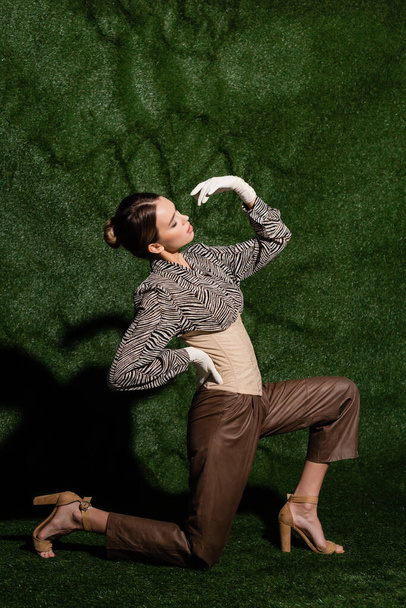 Полная длина стильная женщина в блузке с зеброй отпечаток позирует с рукой на бедре при изгибе возле травянистого фона  - Фото, изображение