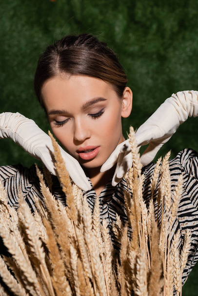 trendy young model in blouse with animal print and white gloves posing near wheat spikelets   - Фото, зображення