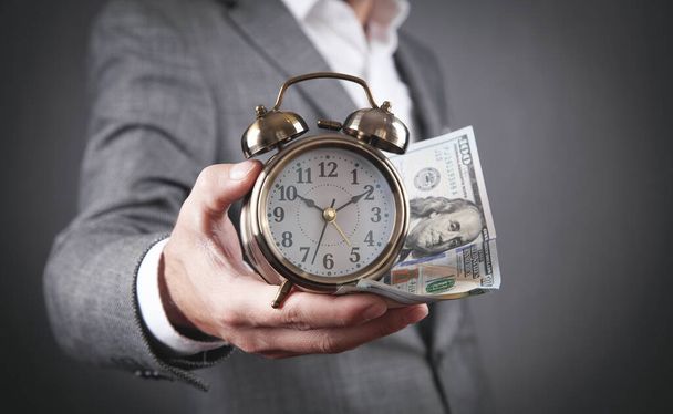 Businessman holding alarm clock and dollar banknotes. - 写真・画像