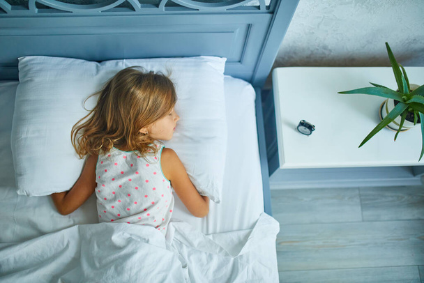 Mała dziewczynka śpiąca na dużym i przytulnym łóżku biała pościel w godzinach popołudniowych w domu, styl życia rodziny, wygodna poduszka, łóżko, zdrowy sen dzieci, melatonina, cycadian rhythms concept - Zdjęcie, obraz