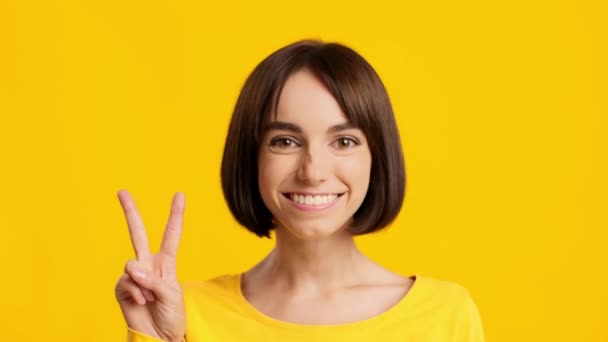 Mujer feliz gestos V-Sign posando sobre fondo de estudio amarillo - Metraje, vídeo