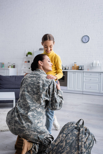 Smiling woman hugging child near military backpack at home  - Фото, зображення