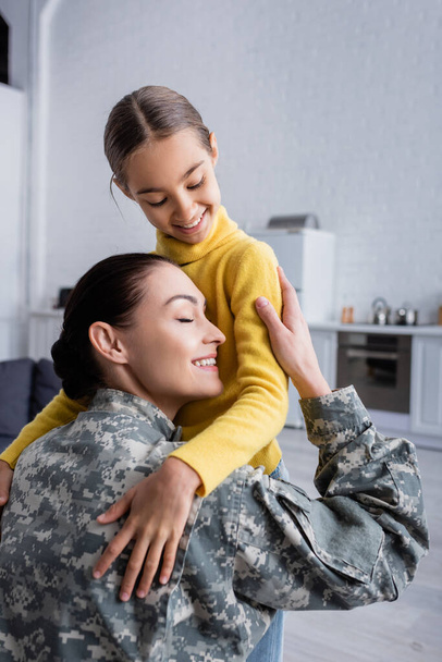 Mãe de uniforme militar abraçando filha em casa  - Foto, Imagem