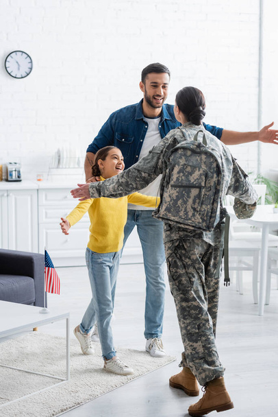 Szczęśliwy mężczyzna i dziecko stojący obok matki w mundurze wojskowym i amerykańskiej fladze w domu  - Zdjęcie, obraz