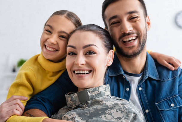 Pozitivní rodina dívá na kameru poblíž matky ve vojenské uniformě doma  - Fotografie, Obrázek