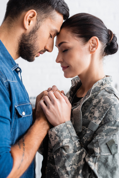 Zijaanzicht van de man hand in hand van de vrouw in militaire uniform thuis  - Foto, afbeelding