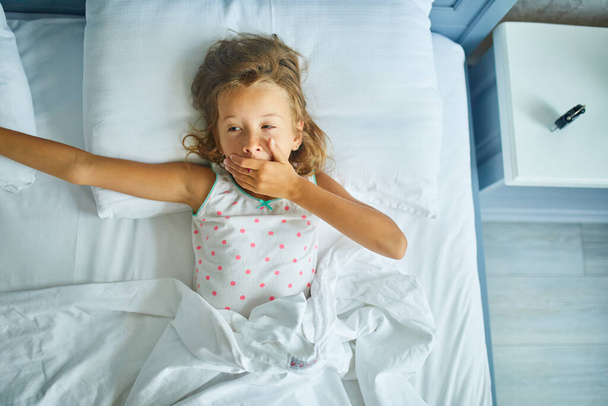 Маленька дівчинка прокидається від сну на великій і затишній постільній білизні вдома, сімейному способі життя, зручній подушці, ліжку, Доброго ранку
 - Фото, зображення