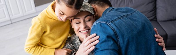 Glückliche Frau in Militäruniform umarmt Ehemann neben Tochter zu Hause, Banner  - Foto, Bild