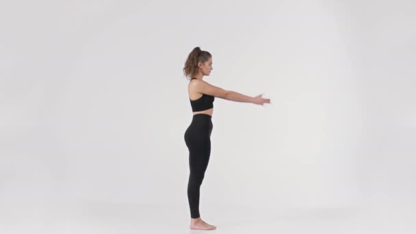 Jovencita vestida con traje negro demostración Utkatasana yoga pose, levantando la mano y haciendo sentadilla, retrato de cuerpo entero - Metraje, vídeo