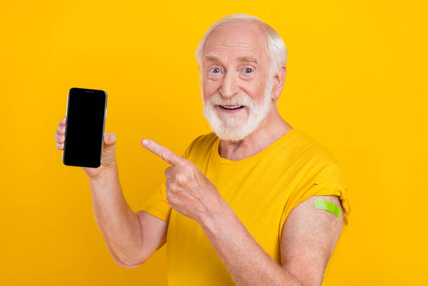Photo of retired promoter man hold phone touchscreen direct sign finger wear t-shirt isolated yellow color background - Foto, Imagem