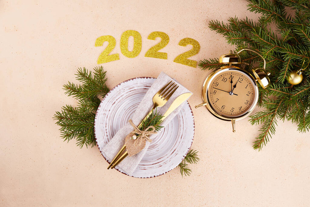 Happy New Year 2022. Festive table setting. Plate, silverware, fir branches, golden alarm clock.  - Photo, image