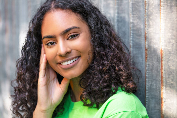 Outdoor portret van mooie gelukkig gemengd ras Afro-Amerikaanse meisje tiener vrouwelijke jonge vrouw denken en glimlachen met perfecte tanden in een stedelijke stad achtergrond - Foto, afbeelding