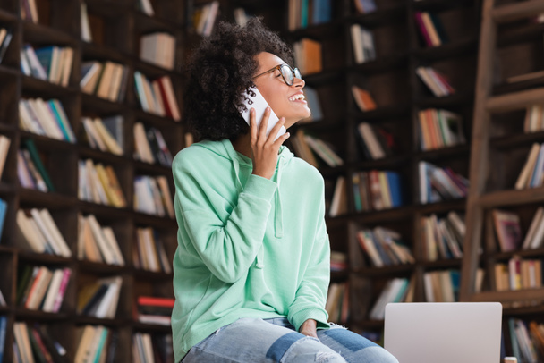 cheerful african american student in eyeglasses talking on cellphone near laptop  - Photo, Image