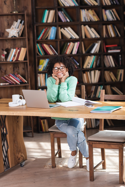 happy african american student in eyeglasses sitting at desk with gadgets  - Photo, image
