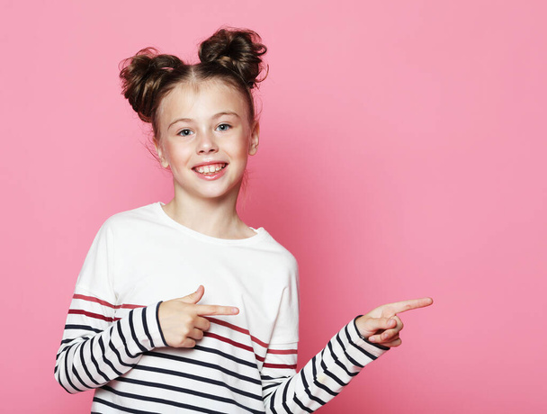 Smiling child girl pointing with finger at blank copy space aside over pink background, lifestyle and education concept - Fotó, kép