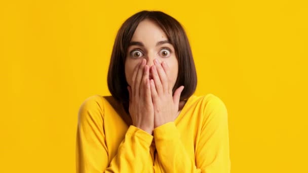 Mujer mirando a la cámara en la boca cubierta de choque, fondo amarillo - Metraje, vídeo