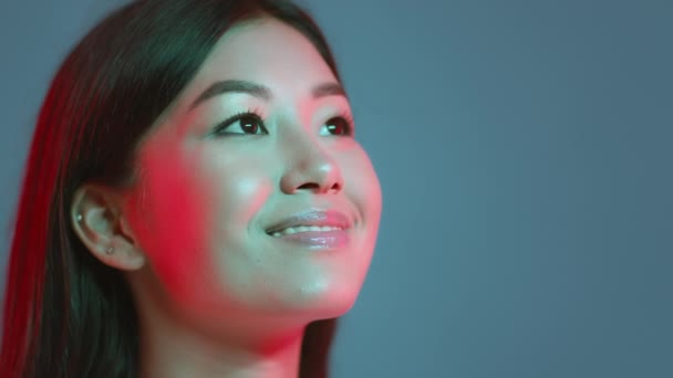 Giovane bella donna asiatica guardando lo spazio libero e sorridendo sinceramente, esprimendo ispirazione, sfondo blu studio - Filmati, video