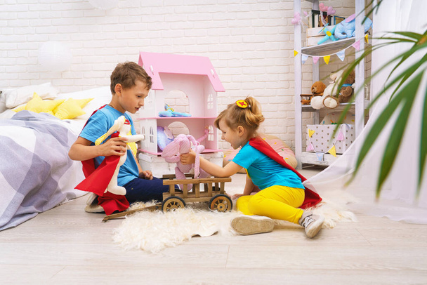 Funny children play with toys in superheroes, in children room. Kids play superhero with Cape and mask at home, saving world and fighting evil. concept protectors and saviors in person small child. - Фото, зображення
