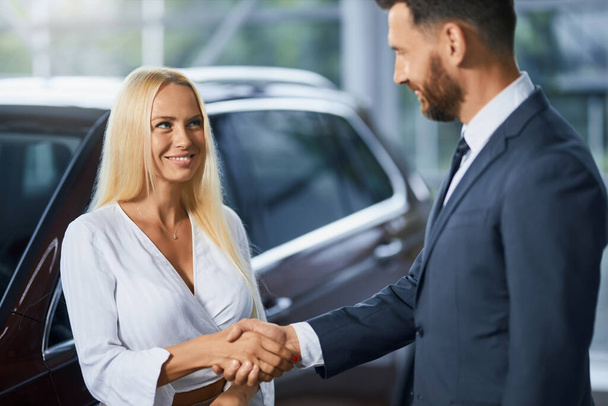 Car dealer shaking hands woman after car purchase - Foto, afbeelding