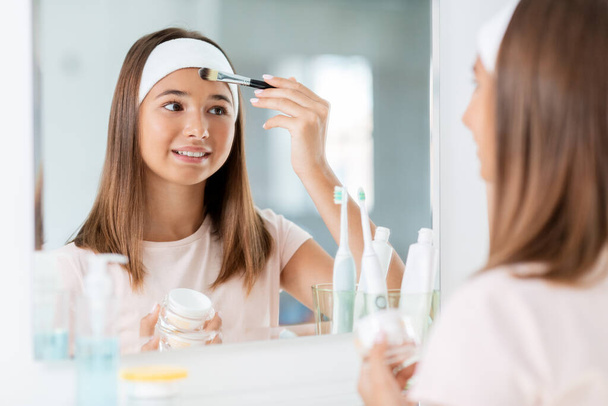 teenage girl applying face mask at bathroom - Фото, изображение