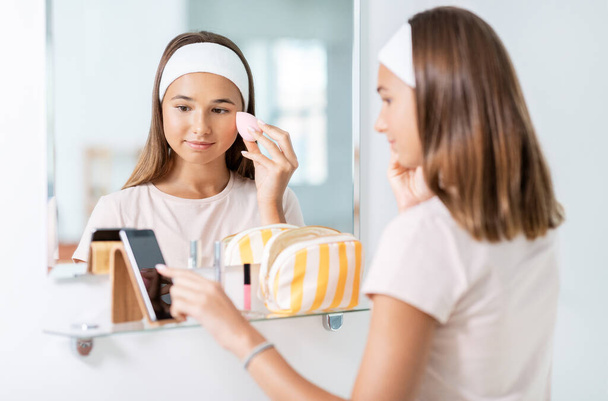 teenage girl with smartphone using make up sponge - Fotografie, Obrázek