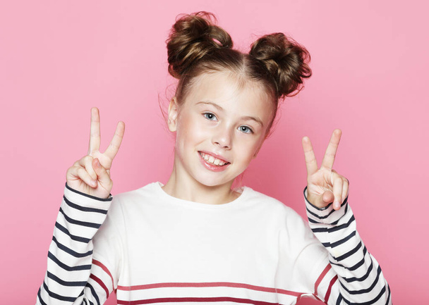 Lifestyle, childhood, emotion and children concept: Close-up portrait of child girl laughing with toothy smile and show v-sign over pink background. - Photo, image