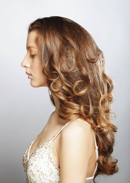 Blonde female model with long and volume shiny wavy hair. Woman with curly hairstyle wearing white dress over grey background. - 写真・画像